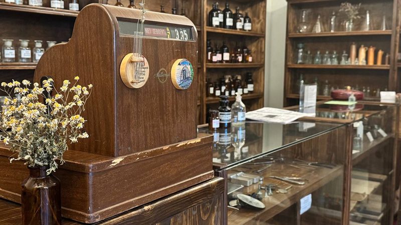 Деревянная касса National на прилавке аптеки, за ней полки с аптечными флаконами