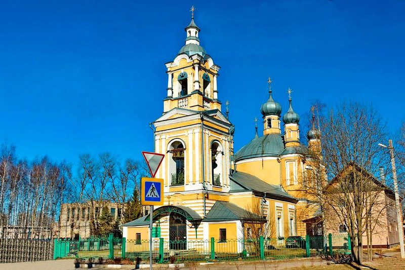 Ильинская церковь в Старице: колокольня и купола на фоне синего неба, перед храмом зелёная ограда